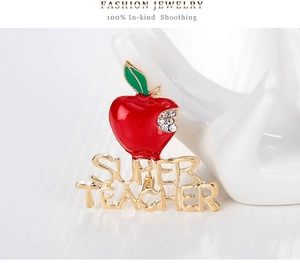 Macro detail of enamel apple brooch with SUPER TEACHER text on a ceramic hand display