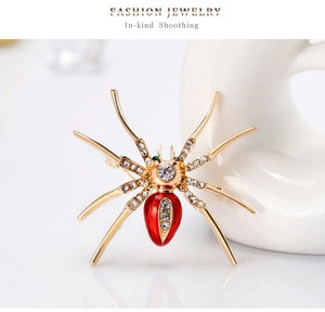Detailopname van een vergulde spinnenbroche met rood emaille en witte strass-steentjes