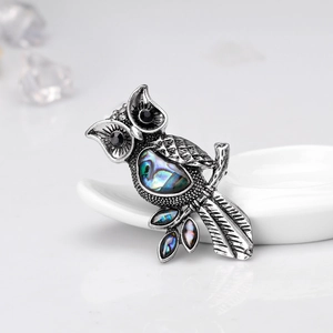 Close-up of vintage owl brooch featuring natural abalone shell on white ceramic tray