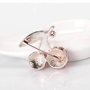 Exquisite cherry brooch in rose gold finish with secure pin back on white porcelain tray