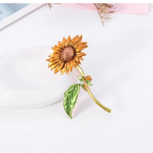 Élégante broche tournesol avec pétales en émail orange doré et feuilles vertes sur fond blanc