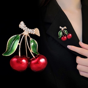 Détail d'une broche cerise en émail rouge et strass portée sur un revers de veste