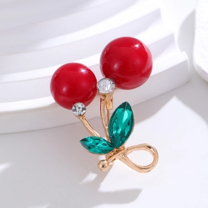 Macro detail of red cherry brooch with sparkling rhinestones and green crystal leaves