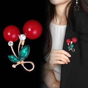 Macro detail of red cherry brooch with crystal leaf on a woman's black blazer