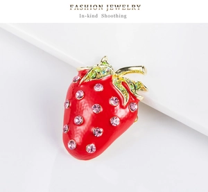 Vue macro d'une broche fraise en émail rouge et cristaux verts sur alliage doré