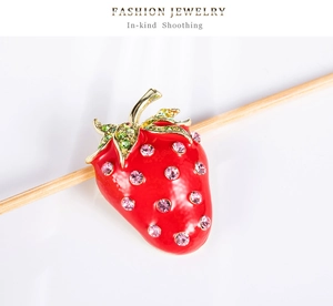 Détail macro d'une broche fraise en émail rouge avec des strass roses incrustés brillants