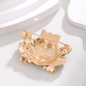 Elegant gold frog brooch with green enamel finish and secure pin clasp on a white stand