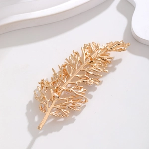 Elegante spilla a piuma dorata con perle su sfondo bianco dallo stile minimal