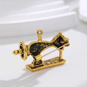 Vintage gold sewing machine brooch with rhinestones and antique finish on a white stand