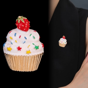 Détail de la broche cupcake fraise avec base dorée et émail coloré sur fond noir élégant