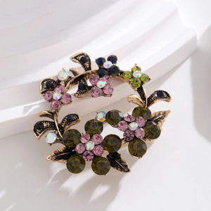 Vintage olive branch wreath brooch with colorful rhinestones on a white pedestal