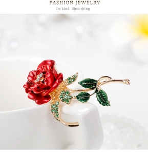 Detailed close-up of a red rose brooch with green crystals hanging on a white cup