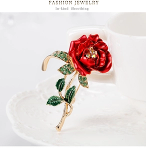 Detailed macro view of a red enamel rose brooch with green rhinestones on a white ceramic cup