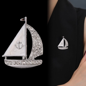 Détail macro d'une broche voilier en émail blanc sertie de strass brillants argentés