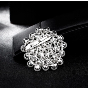 Élégante broche ronde argentée avec perles blanches et strass sur un fond texturé