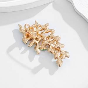 Elegant gold leaf branch brooch with colorful enamel finish shown on a stone tray