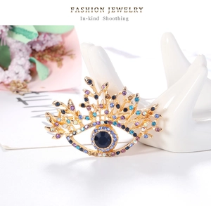 Détail d'une broche en forme d'œil doré avec strass bleus sur un support à bijoux