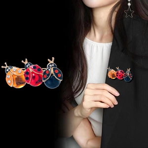 Tre spille a forma di coccinella colorata con strass su un blazer nero