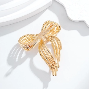 Elegant gold bow brooch with textured twisted wire design on a white minimal stand