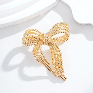 Elegant gold bow brooch with woven twisted metal texture on a minimalist white background