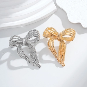 Elegant gold and silver bow brooches with textured metallic design on white podium