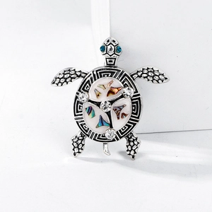 Vintage turtle brooch with shell inlay and blue crystal eyes on a white pedestal