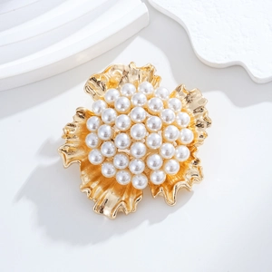 Détail d'une broche fleurie dorée sertie de perles élégantes sur un support blanc épuré