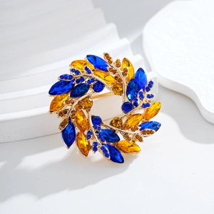 Élégante broche couronne dorée avec strass bleus et ambrés sur un piédestal blanc