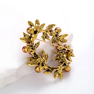 Vintage gold metal leaf wreath brooch with brown pearls on a white stone base