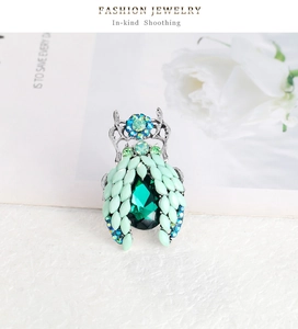 Close-up of beetle brooch featuring dark green gemstone and mint green crystal details