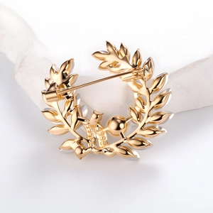 Broche couronne de feuilles dorées avec perles pour manteaux sur fond blanc épuré