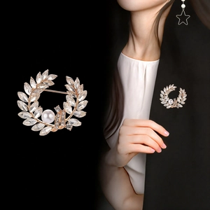 Broche couronne de feuilles dorées avec strass brillants et une perle blanche centrale