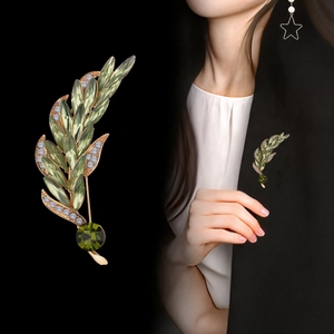 Elegant gold wheat brooch with green crystals and rhinestones shown on black suit jacket
