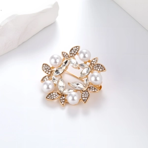 Detailed close-up of a gold wreath brooch with white pearls and sparkling rhinestones