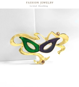Dettaglio della spilla a maschera con finitura dorata, smalto verde e viola e cristalli