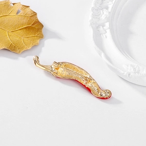 Elegante broche de chile rojo con acabado dorado y pedrería sobre un plato blanco