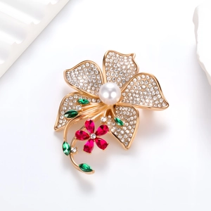 Elegant gold flower brooch with white pearl and crystal petals on white stone surface