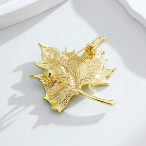 Back view of gold maple leaf brooch with fine texture and pin clasp on white background