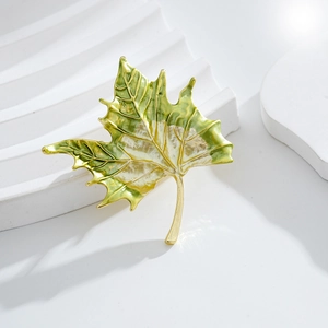 Exquisite gold-edged green enamel maple leaf brooch displayed on a white podium base