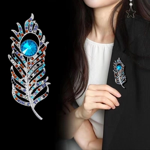 Elegant silver feather brooch with colorful crystals and blue main stone on black blazer