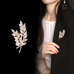 Gold leaf brooch with marquise crystals and round pearl shown on suit and black background