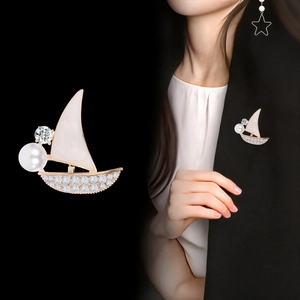 Elegant gold sailboat brooch with white enamel, pearls and rhinestones on a blazer