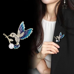 Elegant hummingbird brooch with blue enamel wings, zircons and a pearl on black background