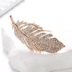 Elegant gold feather brooch with sparkling rhinestones on a minimalist white stone base