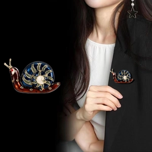 Broche escargot en émail aux motifs spirales bleus sur le revers d'un tailleur noir