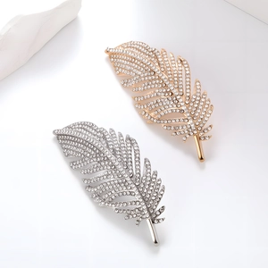 Elegant gold and silver feather brooches with micro-pave crystals on stone backdrop