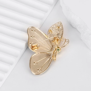 Broche papillon dorée avec des ailes en filigrane et un détail de pierre précieuse verte
