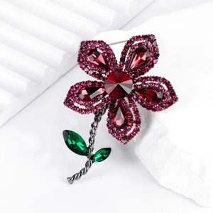 Broche fleur vintage avec pétales en cristal rouge et feuilles vertes sur métal sombre