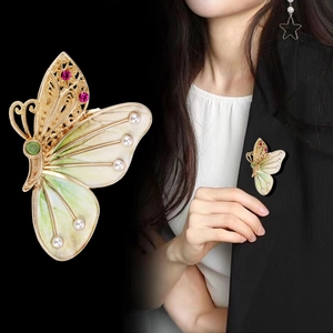 Broche papillon dorée avec gemmes roses et perles portée sur un revers de veste noir