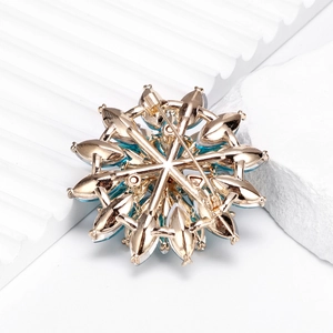 Luxury snowflake brooch with blue crystals and gold metal finish on white stone background